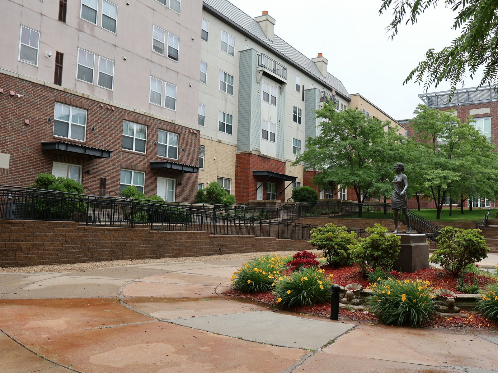 Residential courtyard with landscaping, walking path, and a bronze statue under an overcast sky
